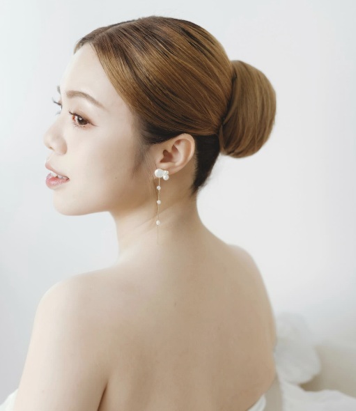 Natural bridal makeup with pearl earrings and a low bun